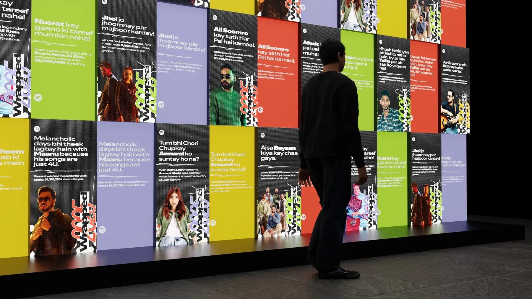 A visitor walking past a wall of colourful Wrapped story cards.