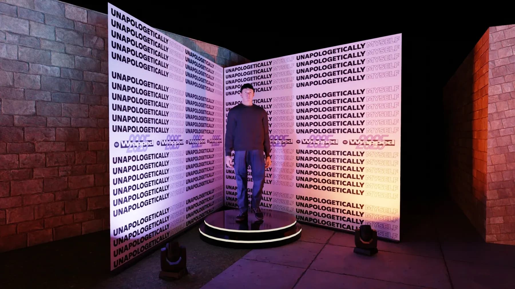 A figure standing on a round podium in front of a wall printed with the word Unapologetically, beside a brick wall.